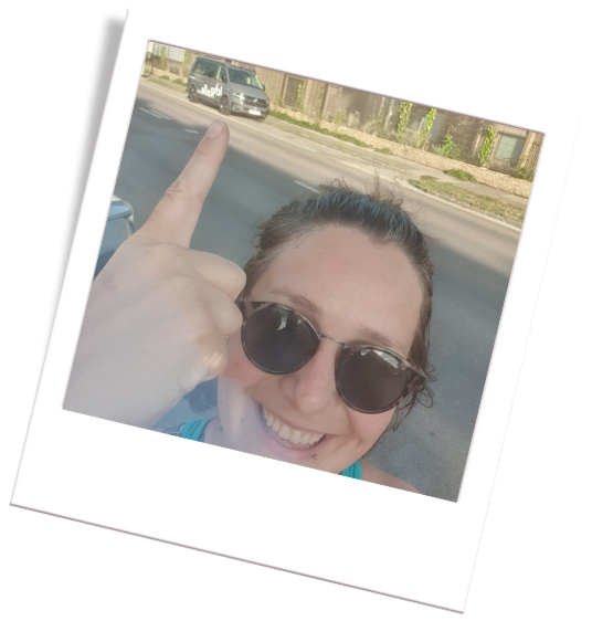 Camper Polaroidfoto. Im Vordergrund einer Frau mit Sonnenbrille, die auf einen Campingbus im Hintergrund zeigt.