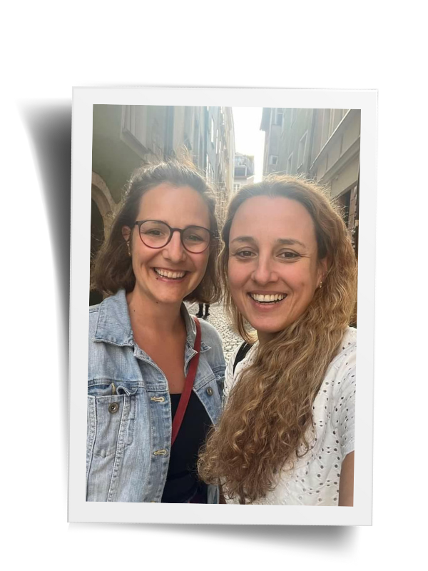 Selfie von zwei lächelnden Frauen im Hintergrund eine schmale Strasse der Regensburger Altstadt. 